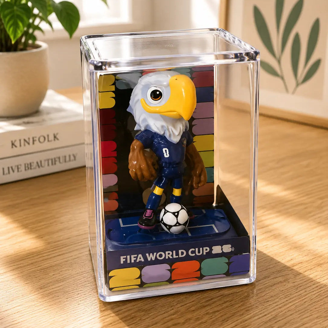 FIFA World Cup figurine in a clear display case on a wooden surface with books and a plant in the background.